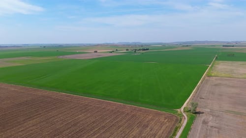 Pedestal drone shot of agriculture pattern, green and brown fields under a cloudy sky on a nice day