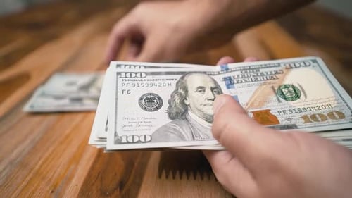 Counting on hundred dollar bills and putting them on a wooden table