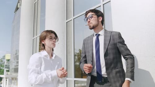 Young Professionals Smoking and Discussing Ideas While Standing Outside a Modern Office Building on