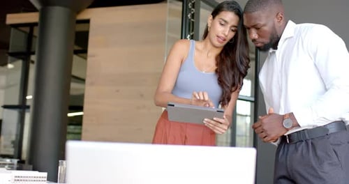 Discussing project details, diverse colleagues using tablet in modern office setting