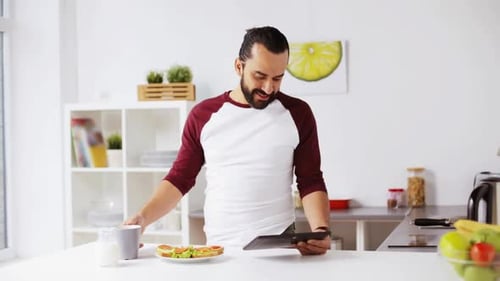 Man Uses Tablet, Drinks Coffee, and Eats Breakfast