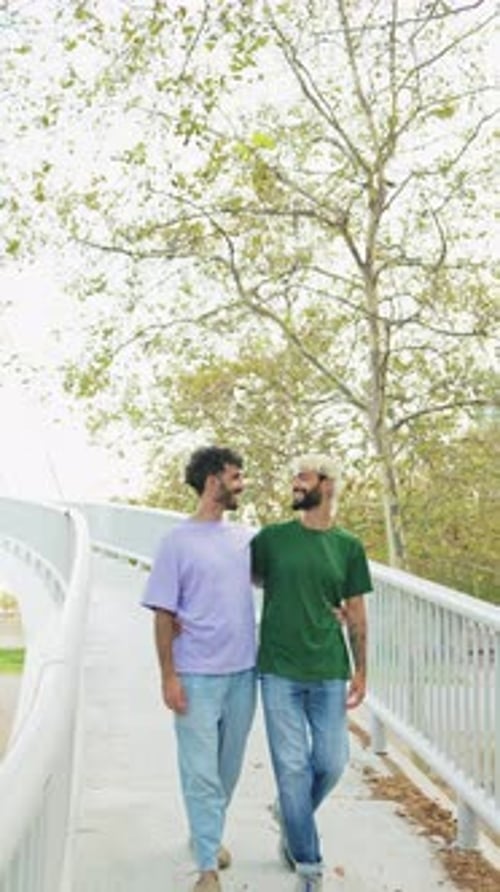 Vertical of a young gay couple in love walking together embracing in a park in daylight