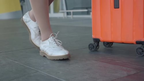 Mulher andando no aeroporto em meias de compressão com mala rolante laranja