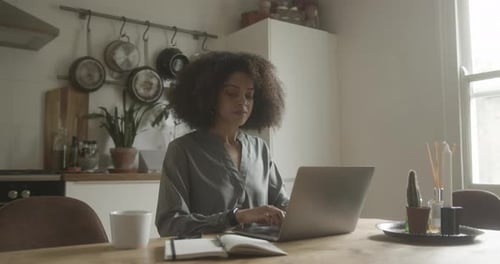 Woman Working On Laptop At Kitchen Table
