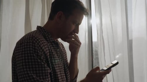 Man Contemplates Phone News By Bright Window