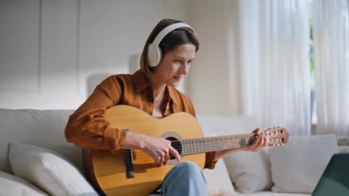 Woman Plays Guitar on Couch with Headphones