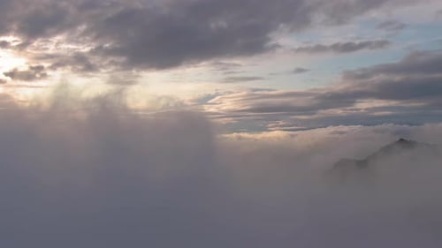 Beautiful Sunset aerial flying over clouds above foggy mountain peak