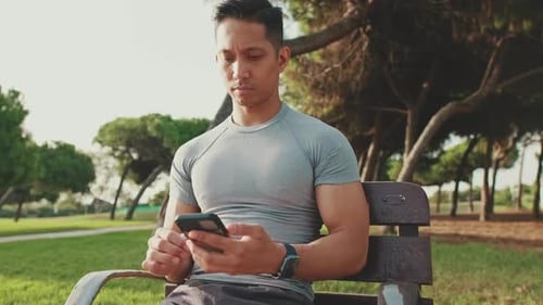Young man sitting on a park bench uses a mobile phone