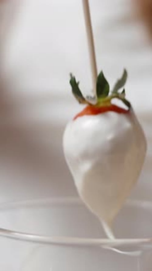 Close-up shot of the excess white chocolate dripping off the strawberries. Vertical video.