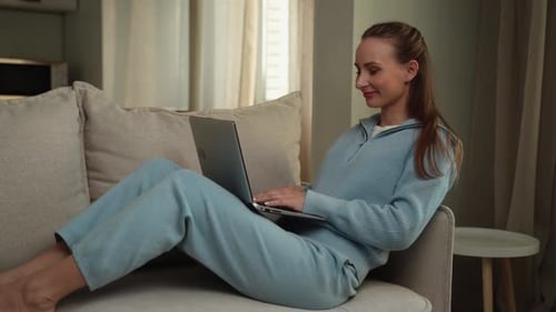 Woman Works on Laptop While Relaxing on Sofa