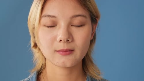 Portrait smiling woman opens eyes and looks at camera isolated on blue backgroundin studio