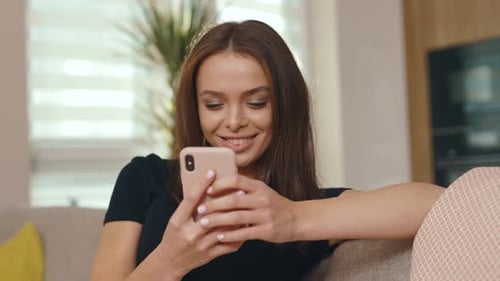 Smiling woman relaxes on sofa using mobile phone