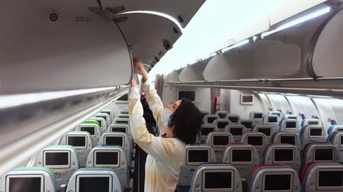 Une femme portant un masque facial ouvre un casier supérieur dans un avion et sort le sac de l'étagère supérieure