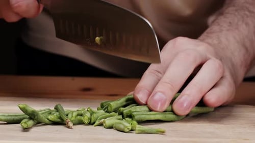 Frische grüne Bohnen mit dem Messer auf einem Holztisch schneiden, eine Grundnahrungszutat liegt auf einem Holztisch