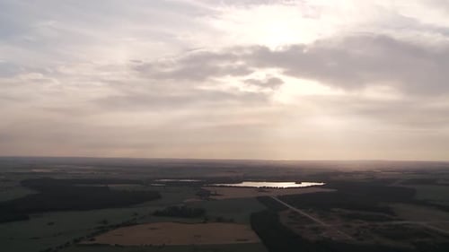 Aerial view of a tranquil lake at sunset with sprawling fields under a cloudy sky
