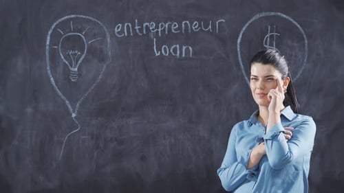 Woman writing entrepreneur loan on blackboard looks up with happy expression.