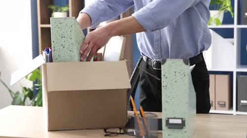 Despido. Hombre empacando sus objetos personales en una caja de cartón en una mesa de madera en la oficina, primer plano