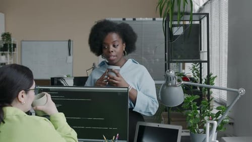 Two Ethnically Diverse Female Programmers Chatting during Coffee Break in Office