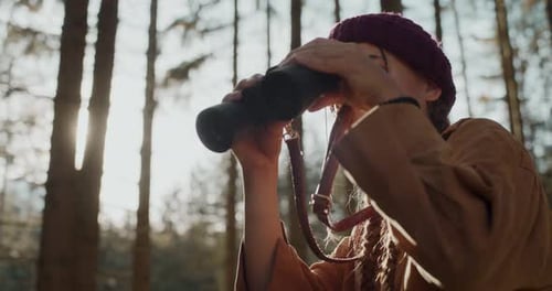 Woman Hiker Uses Binoculars in Forest Sunlight