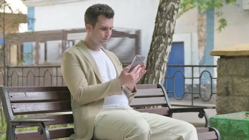 Man Using Smartphone While Sitting on Park Bench
