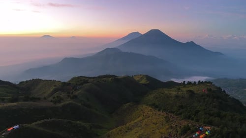 Drone shot of scenic mountain ridges at dawn with volcanoes in the distance under soft sunrise skies