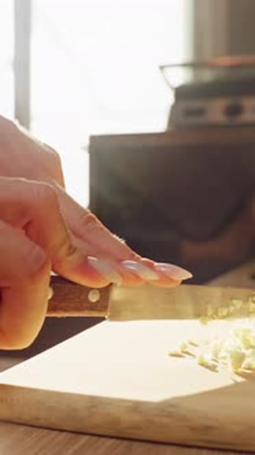 Vertical video. Slow Motion Close Up Of Woman Chopping Garlic With Knife On Wooden Cutting Board In
