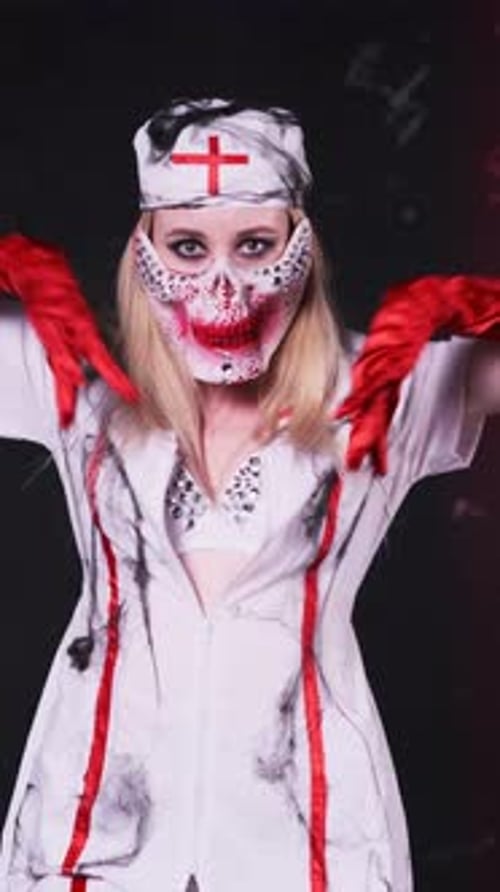 Beautiful sexy girl in scary nurse costume, red gloves and scary mask for Halloween dancing on black