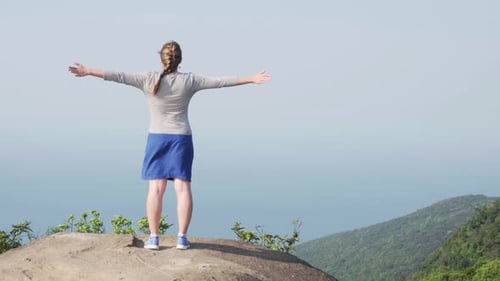 Young woman raising hands on top of mountain