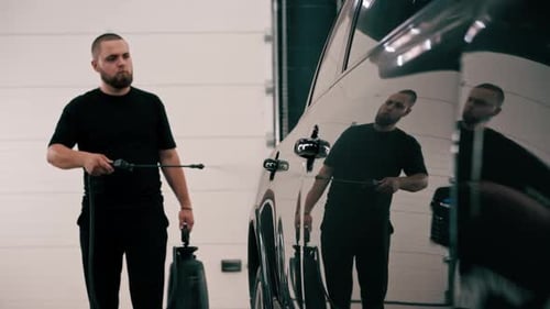 A male car wash employee applies car wash detergent to a black luxury car using spray gun car wash