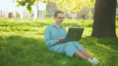 Busy Attractive Woman Working on the Laptop While Sitting on Grass in City Park