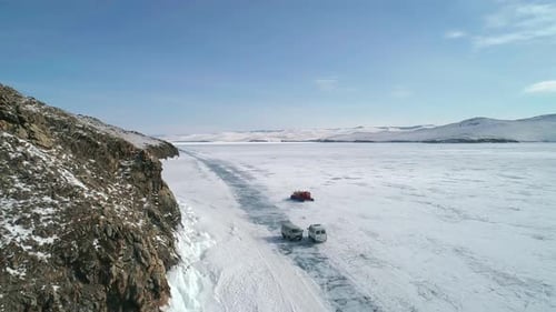 Aerial View on the Hovercraft Driving on Cracked Snowy Ice of Baikal Along the Rocky Cliff Drone