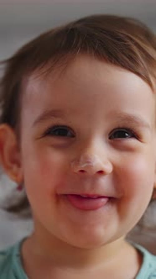 Bambin souriant avec langue tendue à l'intérieur, jeune enfant heureux dans une pièce lumineuse vêtu de bleu sarcelle