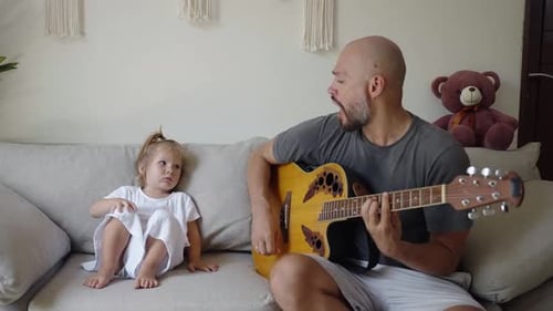 Man Playing Guitar with Little Girl on Couch