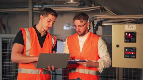 Engineers Collaborating on Industrial Control Panel Maintenance with Laptop