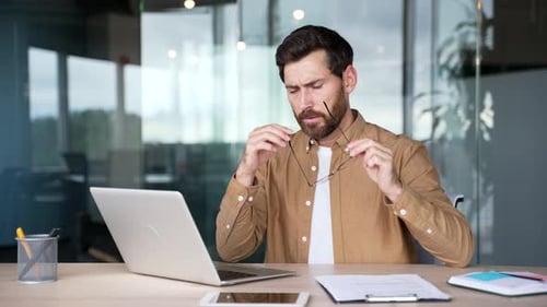 Man Working on Computer in Office Looks Tired