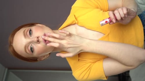 Young Woman Applying Lip Gloss With Finger Indoors