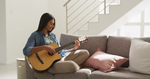 Woman Plays Guitar on Couch in Sunny Room