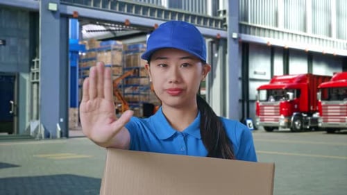 Courrier féminin faisant une halte et secouant la tête tout en livrant un carton, à l'extérieur de l'entrepôt