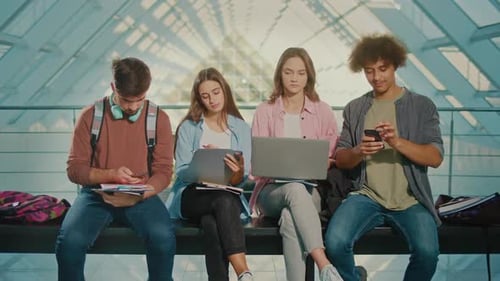 Group of Students Sitting on Bench Typing on Smartphones at University Hall