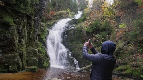 Scenic Waterfall in Forest with Person Taking Photo