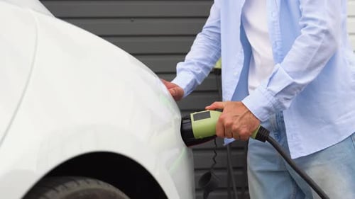 The Driver of the Electric Car Inserts the Electrical Connector to Charge the Batteries Close Up