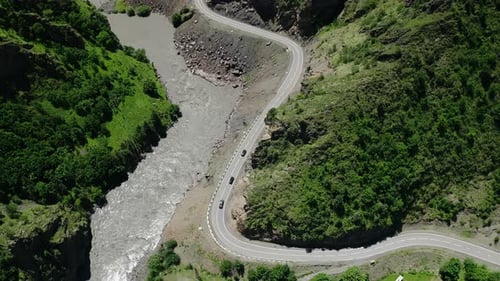Estrada panorâmica de montanha curvilínea ao lado de um rio rápido cercada por uma densa vegetação vista de cima