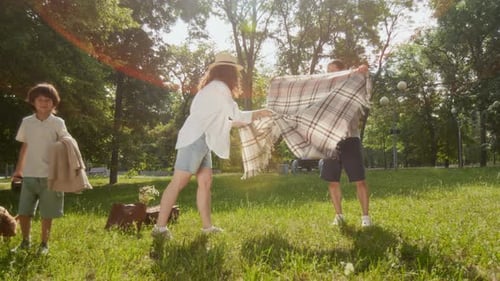 Family of Three Setting Up Blanket for Picnic in Park