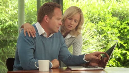 Loving couple use laptop together inside home near window