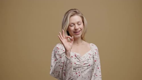 Smiling Woman Gesturing OK With Hand Against Beige Background