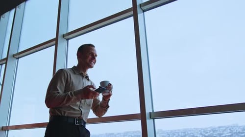 Man Using Phone, Coffee by Office Window