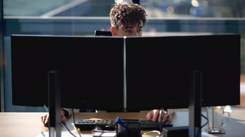 Young man is working in a computer in an office, windows on the background