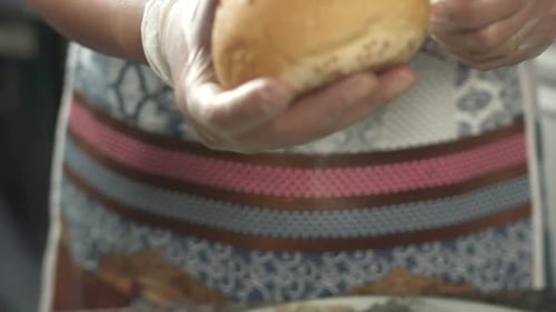 Gloved Person Cuts Sesame Seed Bun in Half