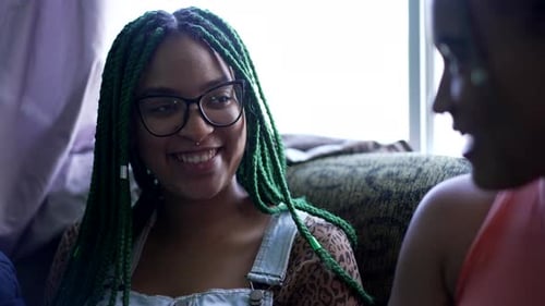 Two Young Women With Braided Hair Laughing and Talking Indoors