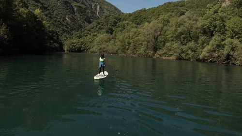 A young sportive girl paddling on a SUP board along a canyon. Picturesque landscape with calm blue w